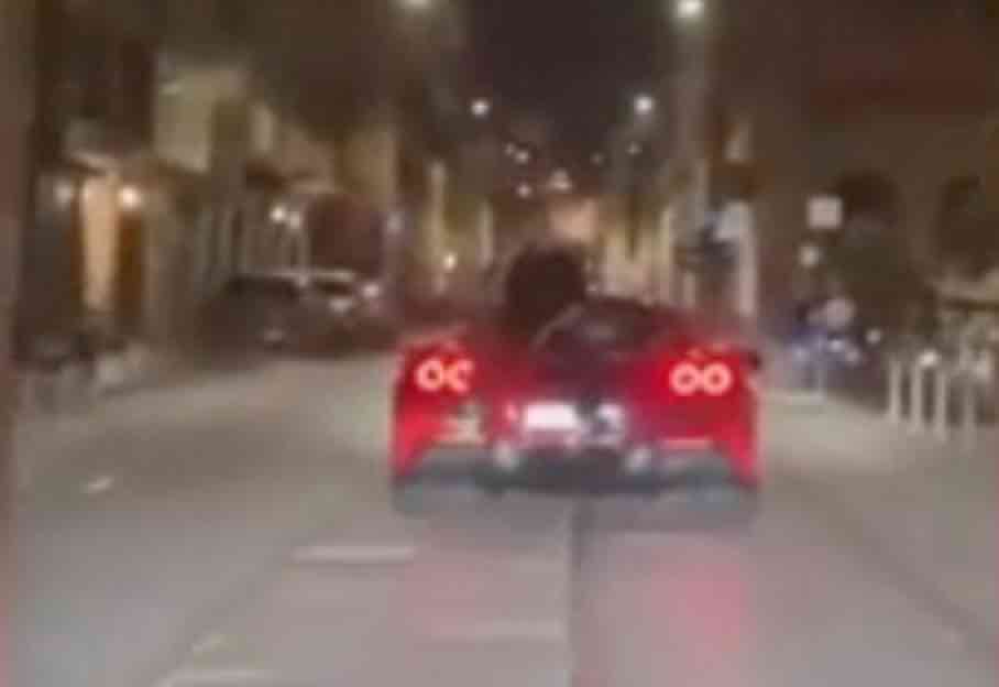 Ragazzo seduto sul cofano di una Ferrari al telefono per le vie di Milano